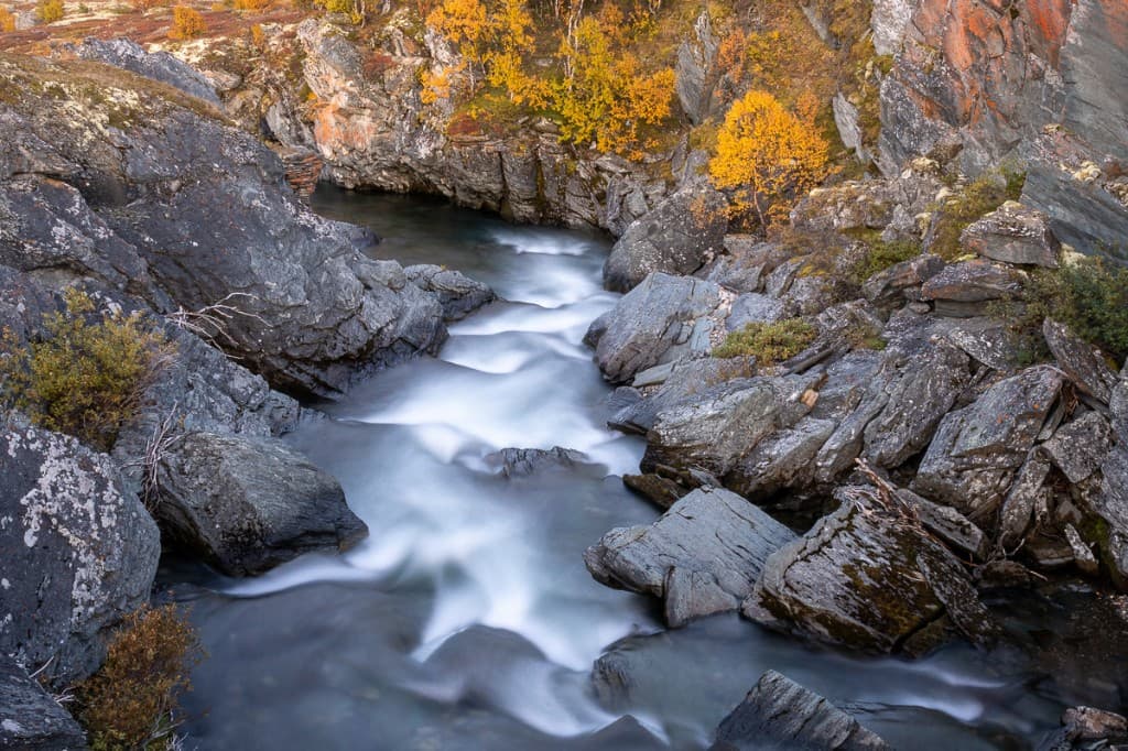 Forsande vatten genom klippformation med höstfärger — Rondane nationalpark