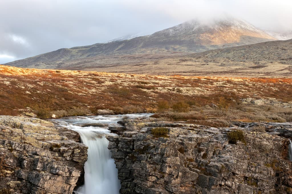 Vattenfall över klippkant med berg i mjukt sidoljus — Rondane nationalpark